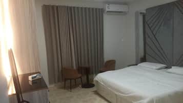 A hotel room with a bed, a desk, a chair, and an air conditioning unit.