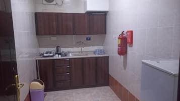 A compact kitchen with a sink, cabinets, a fire extinguisher, and a small refrigerator.