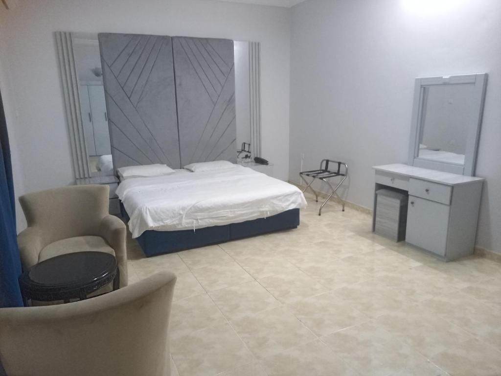 Een slaapkamer met een bed, een stoel, een klein tafeltje, een spiegel en een kast.