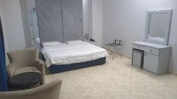 Een slaapkamer met een bed, een stoel, een klein tafeltje, een spiegel en een kast.