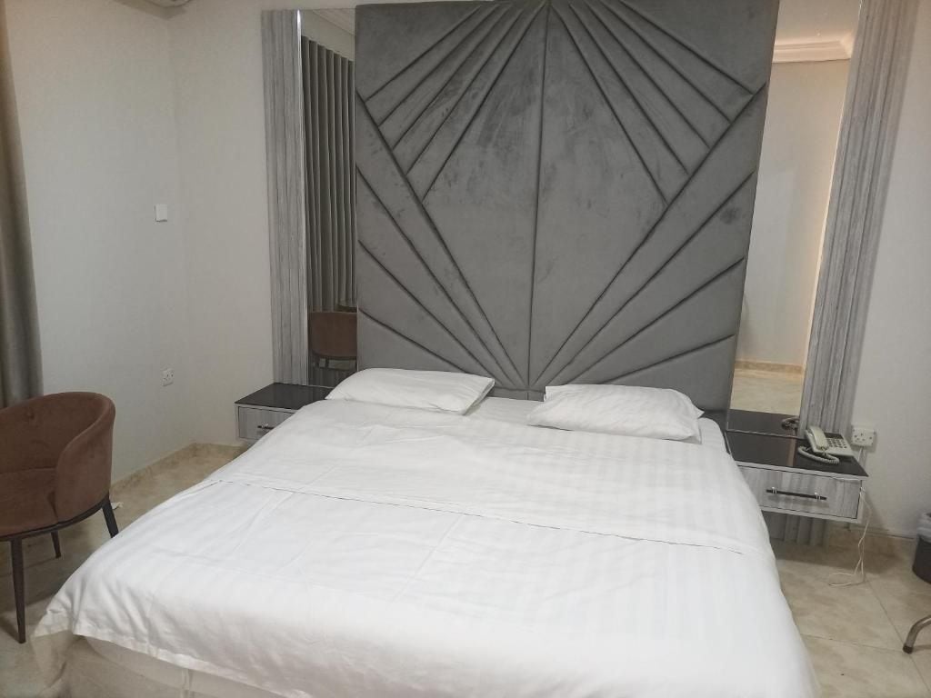 Una habitación de hotel con una cama grande, una mesita de noche con lámpara, una silla y un cabecero moderno.