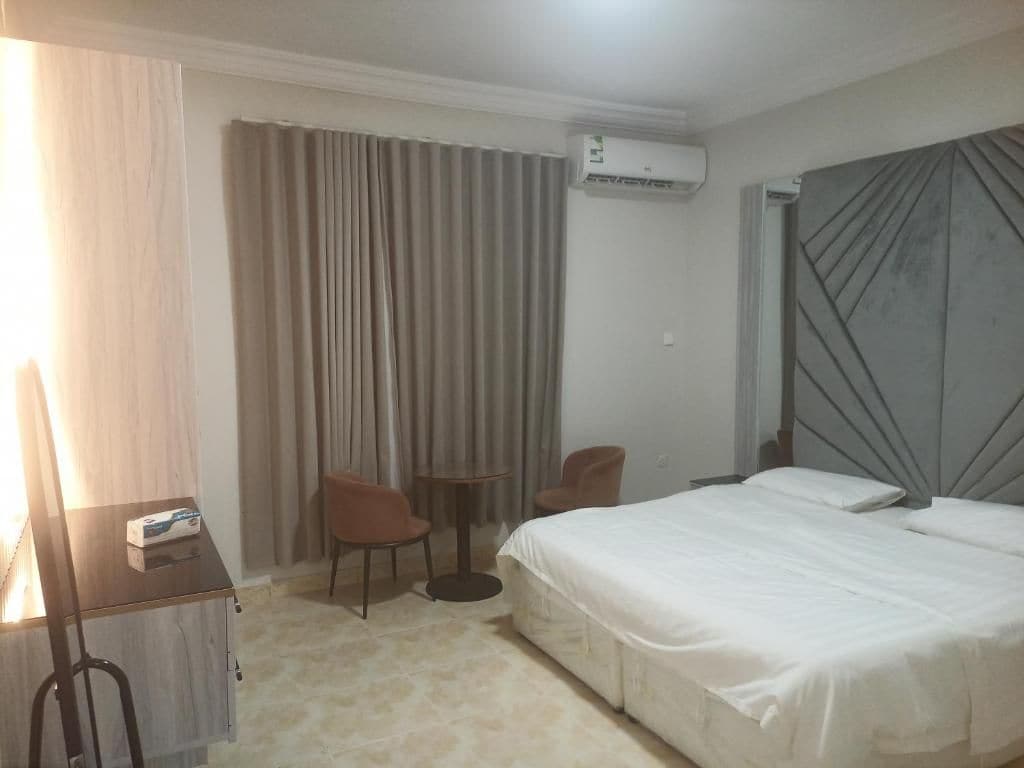 Ein Hotelzimmer mit Bett, zwei Stühlen, einem kleinen Tisch, einer Klimaanlage und einem Vorhang.