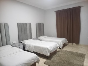 A hotel room with two beds, a nightstand, a lamp, and a brown curtain. - Fouad Ali Al-Ezzi for Serviced Apartments Al-Sail Road (Taif)
