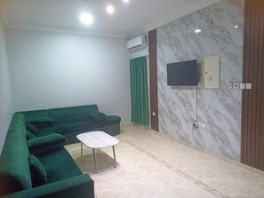 Habitació amb un sofà modular, una taula petita de color blanc, un televisor de pantalla plana al mur i un mur amb dibuix de marbre.