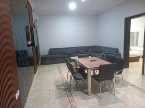 Un saló amb un sofà, una taula de dinar amb cadires i un llit al fons.