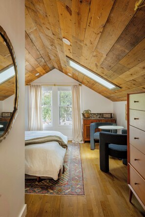 Un dormitorio con techo inclinado, una cama, un aparador, una silla y una mesita.