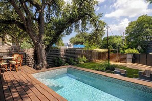 A swimming pool with a wooden deck, surrounded by a fence and trees. - Bangin' Bungalow on South Congress | Heated Pool (Austin)