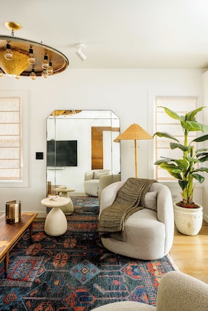 A modern living room with a round chair, a large potted plant, a patterned rug, and a unique ceiling light fixture. - Bangin' Bungalow on South Congress | Heated Pool (Austin)