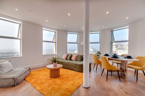 A modern living room with a sofa, a dining table with chairs, and large windows.