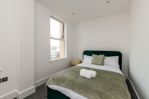 A bedroom with a single bed, a window, and a small bedside table.