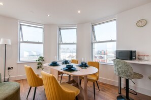 A dining area with a round table, yellow chairs, and a view through large windows.