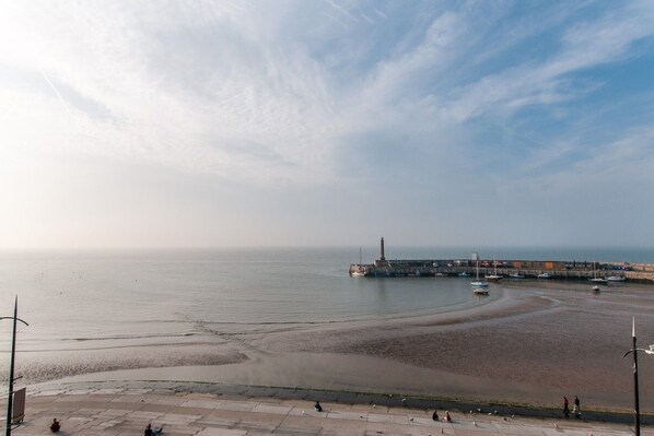 A coastal view with a sandy beach, a pier, and a clear sky.
