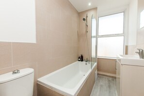 A modern bathroom with a bathtub, toilet, and a window.