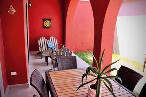 Eine Terrasse im Freien mit einem Holztisch und -stühlen, einem Topfpflanzen und einem Dartbrett an der Wand.