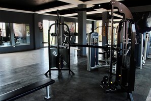 Ein Fitnessraum mit verschiedenen Trainingsgeräten, einer Bank und einer Spiegelwand.