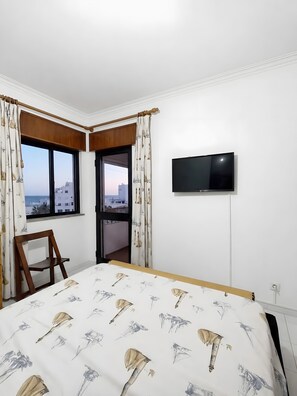 A hotel room with a bed, a TV, a chair, and a window with a view of buildings. - Apartment 'Mar Azul' with sea view, balcony and Wi-Fi (Quarteira)
