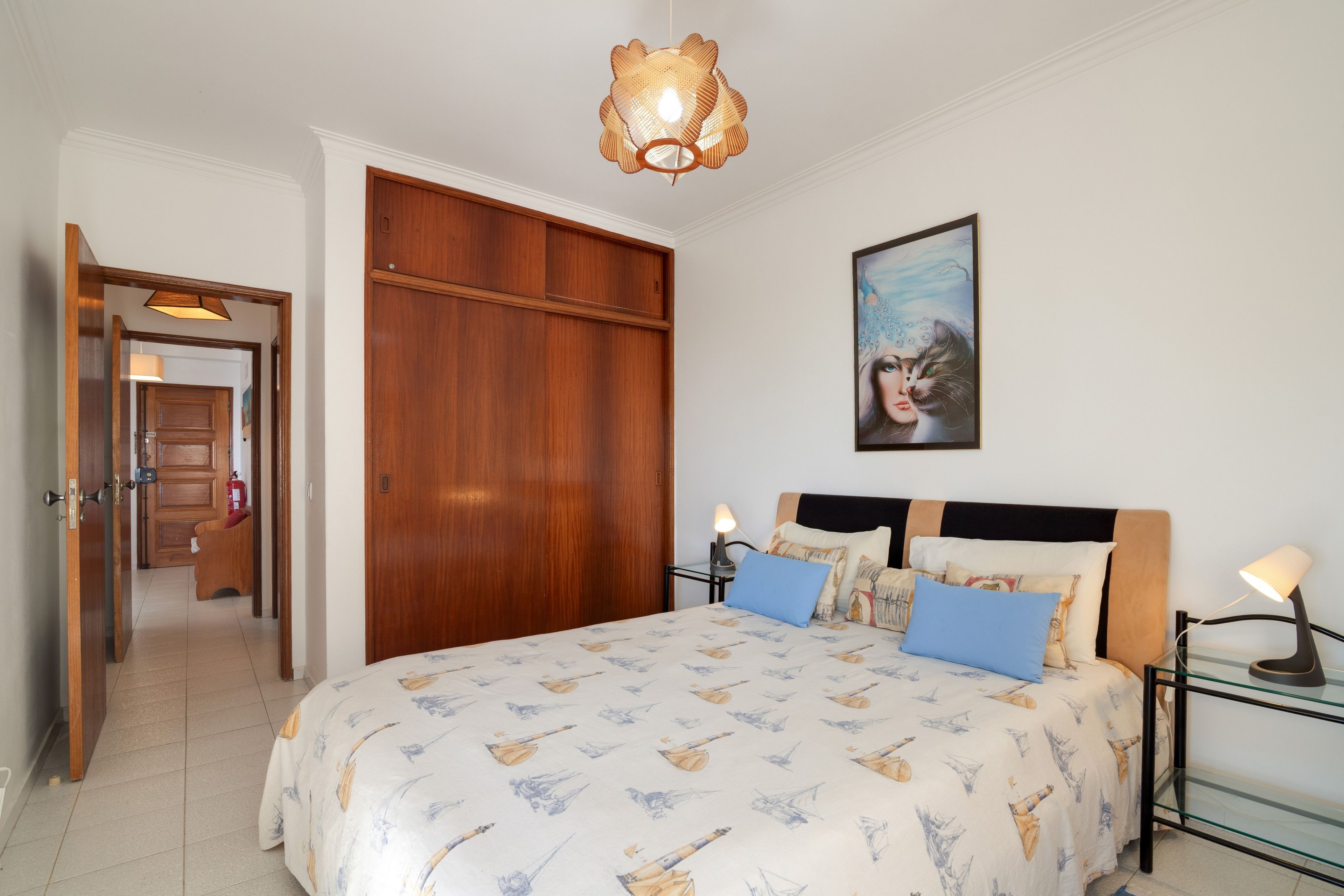 Ein Schlafzimmer mit einem Bett, Nachttischlampen, einem Gemälde und einem Holzschrank.