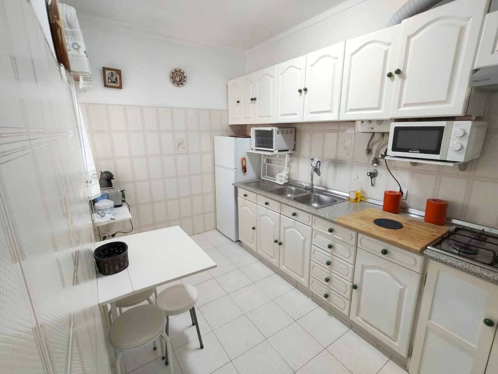 A compact kitchen with white cabinets, a microwave, a stove, and a sink. There is a small table with two chairs.