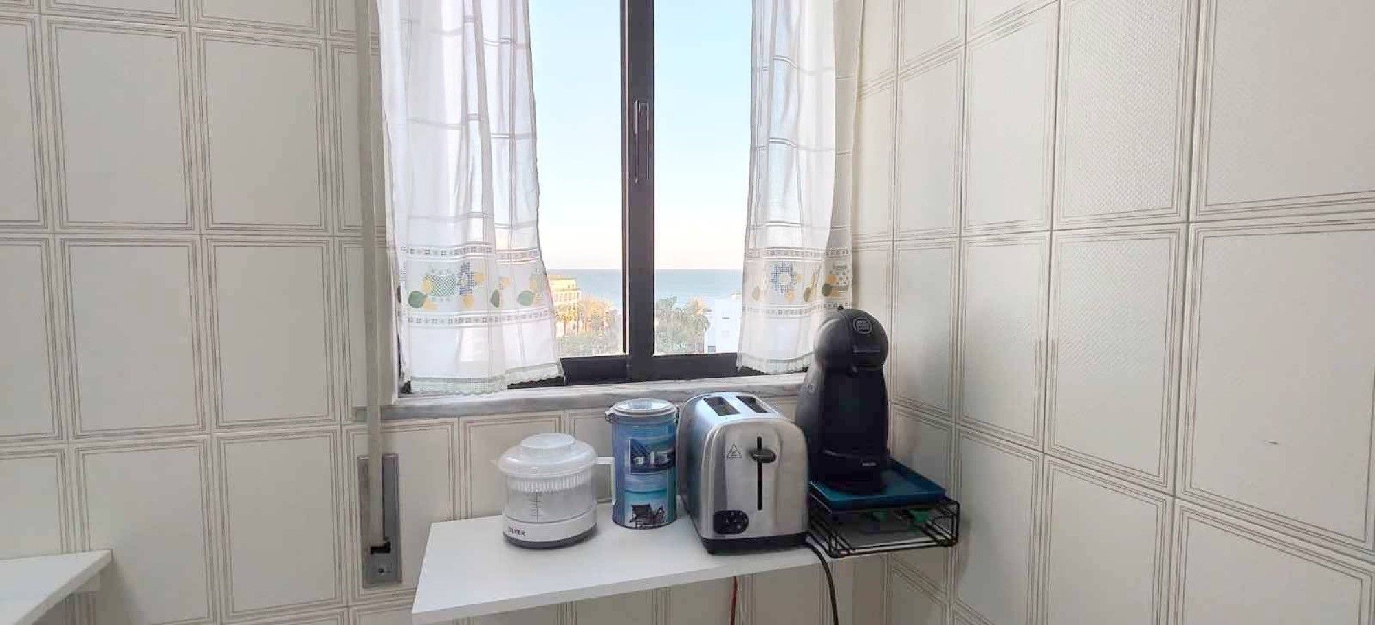 A small kitchenette with a window, a toaster, a kettle, and a water dispenser on a white countertop.