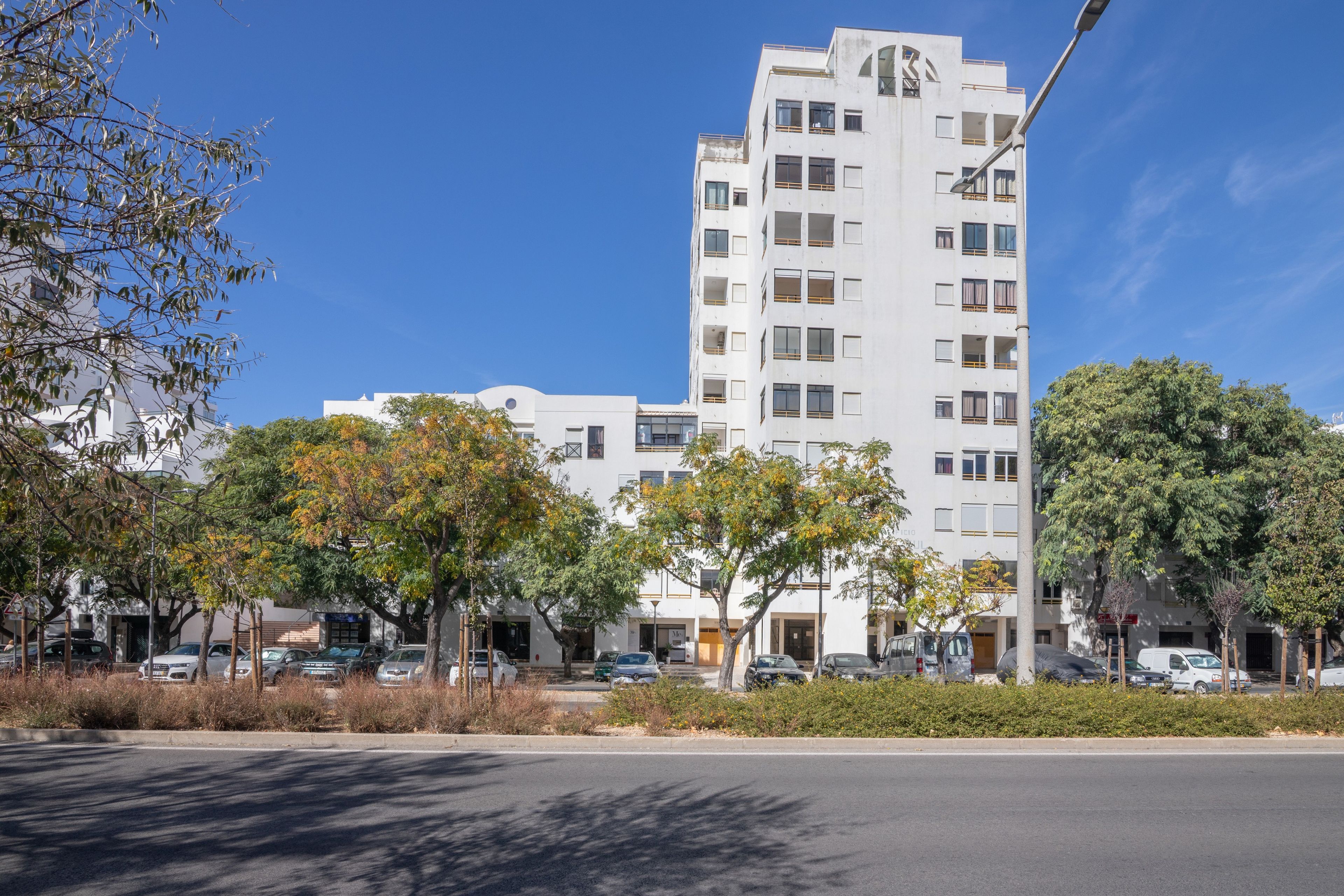 Ein mehrstöckiges Wohngebäude mit einer glatten Fassade, mehreren Balkonen und einem Parkplatz davor.
