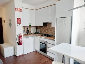 Eine moderne Küche mit weißen Schränken, einem Gasherd, einem Backofen, einem Kühlschrank und einem Feuerlöscher.
