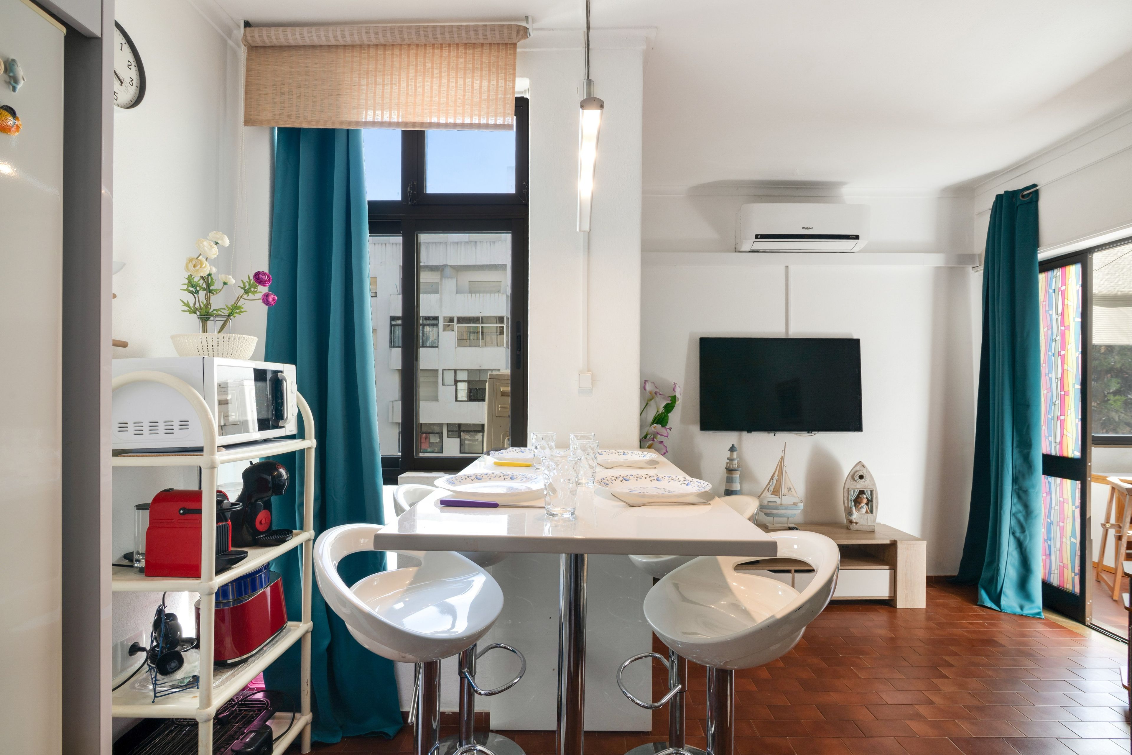 A modern kitchen with a dining table, bar stools, and a large window with curtains.