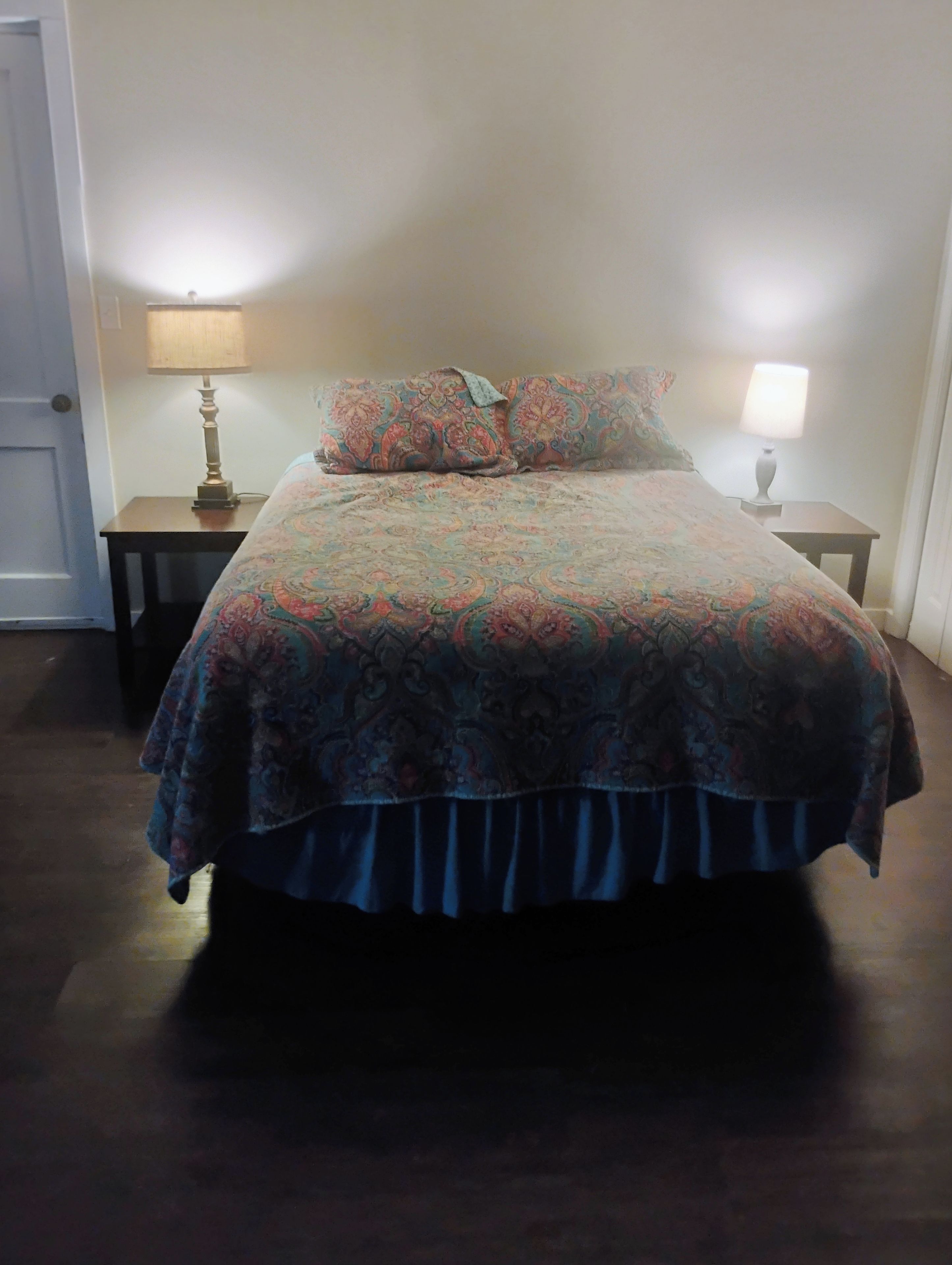 Un lit avec une couvre-lit à motifs et des oreillers, flanqué de deux tables de chevet sur lesquelles sont posées des lampes.