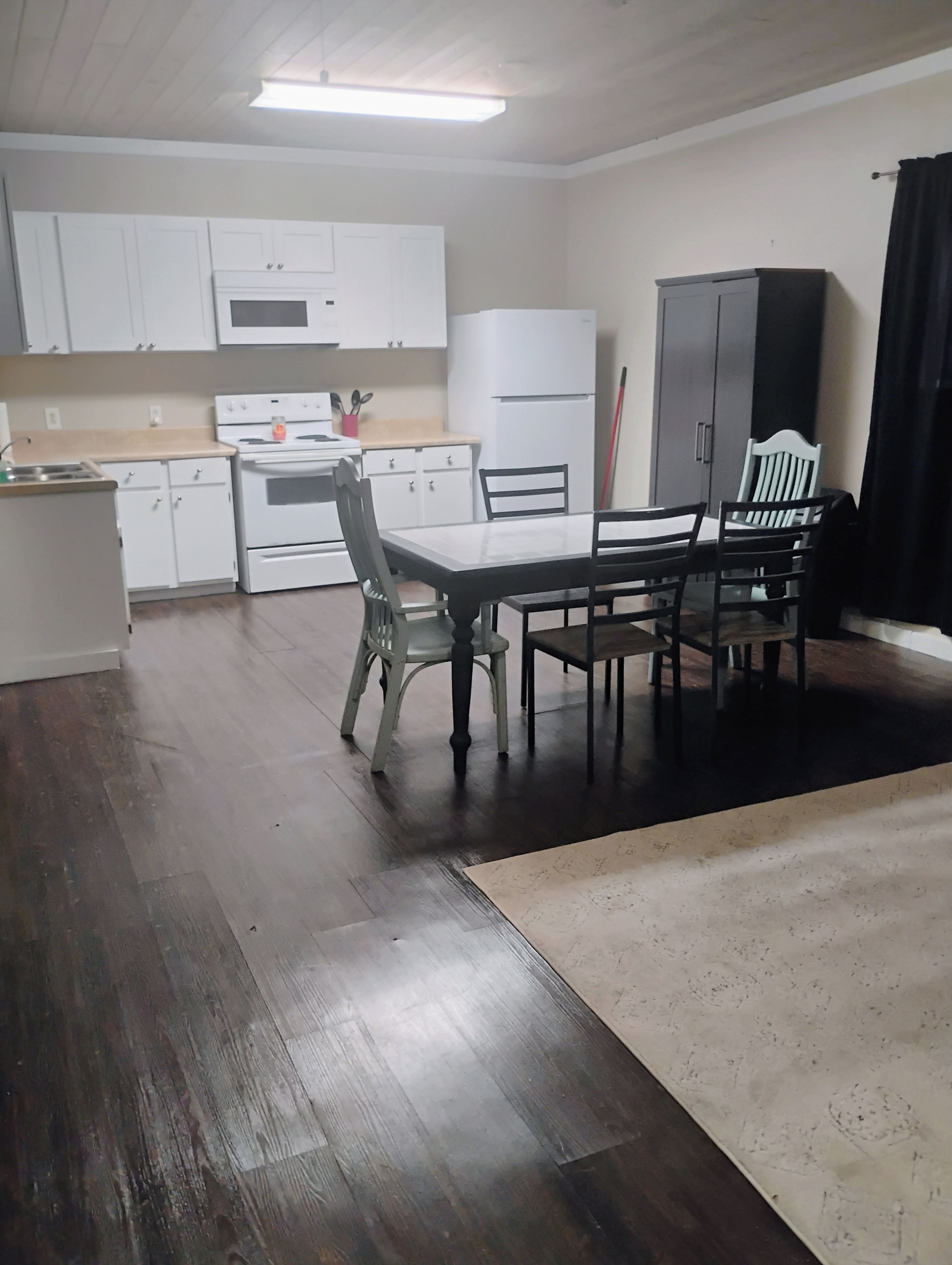 Een keuken met witte kastjes, een fornuis en een eethoek met een tafel en stoelen.