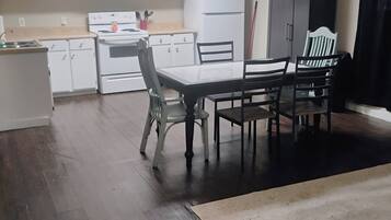 Een keuken met witte kastjes, een fornuis en een eethoek met een tafel en stoelen.