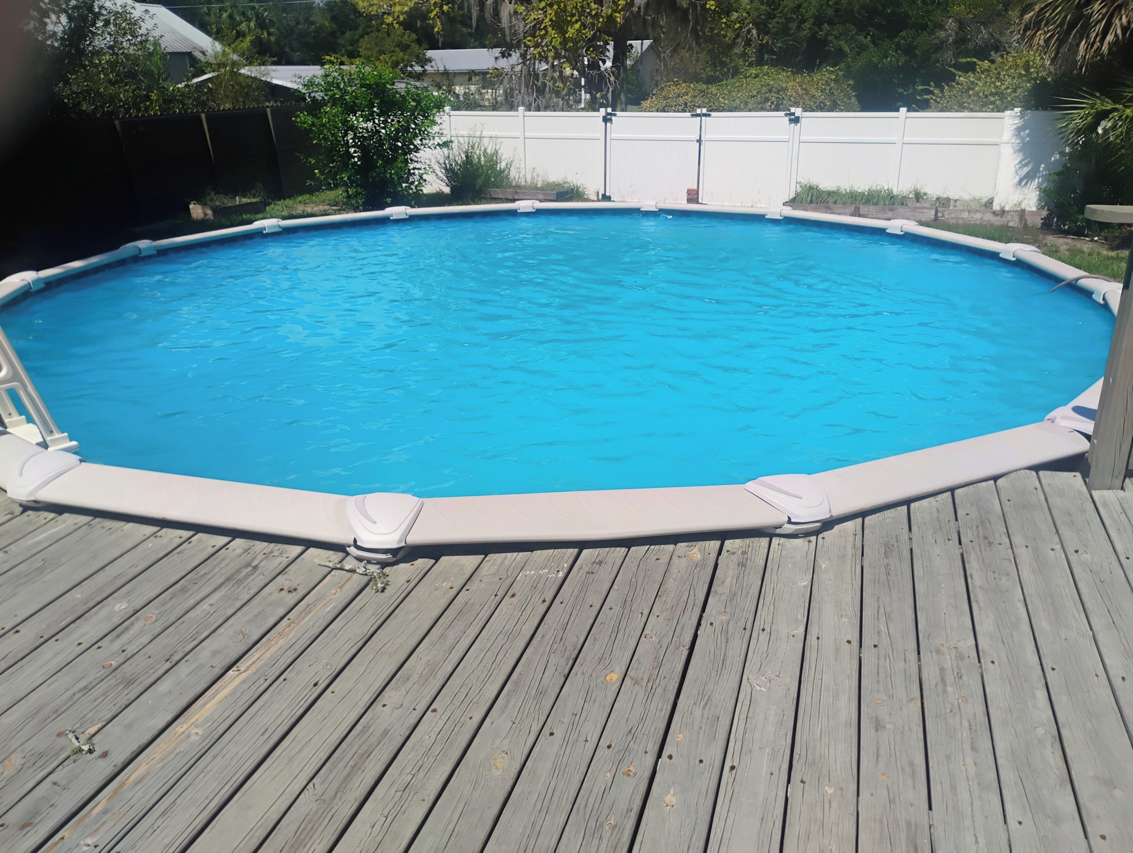 Une piscine rectangulaire hors sol, entourée d’une terrasse en bois.