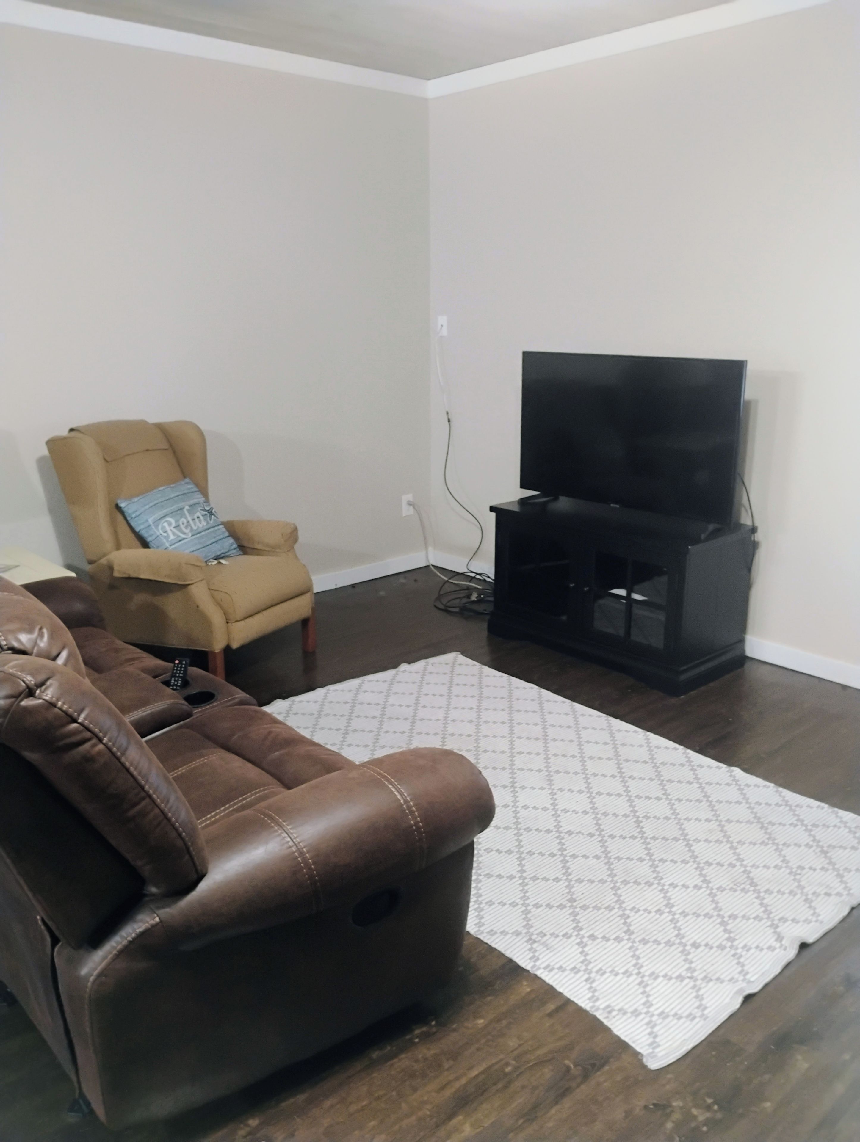 Ein Wohnzimmer mit einem braunen Ledersofa, einem beige Armlehnstuhl, einer schwarzen Unterhaltungsanlage mit Fernseher und einem gemusterten Teppich.