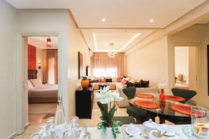 A modern living room with a dining area, a sofa set, and a bed visible through an open door. - Serene 2-bedroom apartment with pool view and private parking (Marrakech)