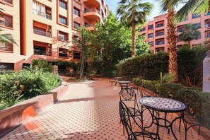 A courtyard with tiled flooring, outdoor seating, and lush greenery. - Serene 2-bedroom apartment with pool view and private parking (Marrakech)