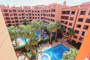 Ein mehrstöckiges Hotel mit Innenhof, der einen Swimmingpool, Palmen und Liegestühle zeigt.