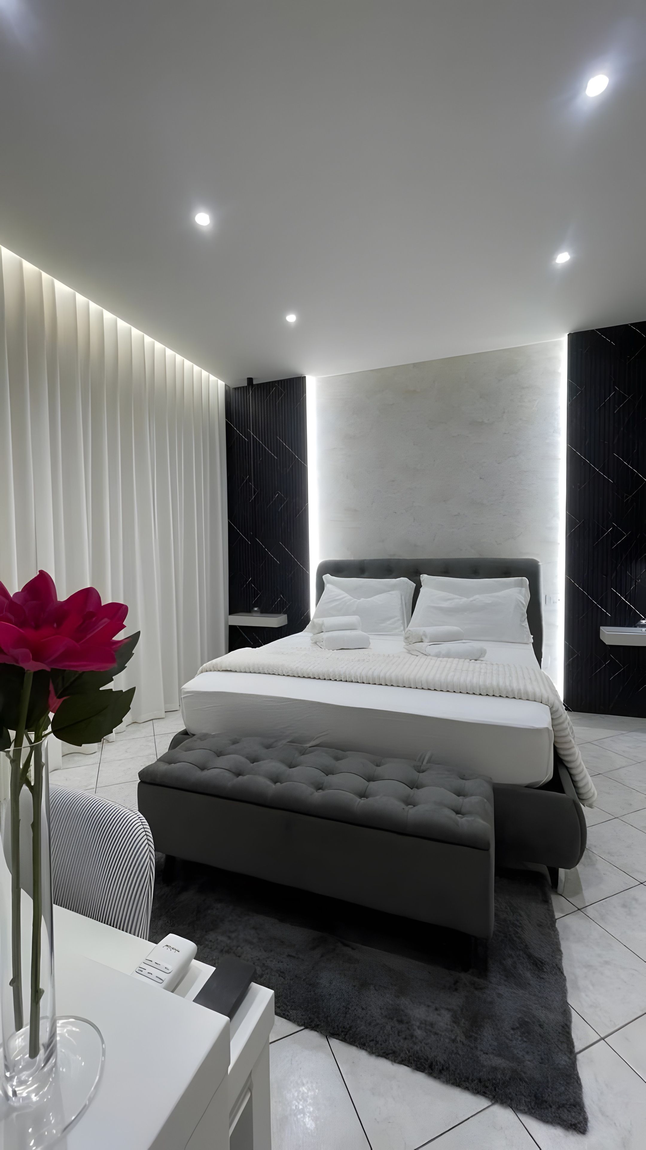 A modern bedroom with a large bed, bedside tables, a bedside lamp, and a decorative vase with flowers.