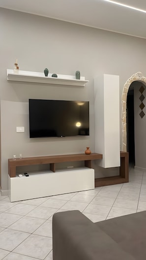 A modern living room with a flat-screen TV mounted on the wall, a wooden entertainment unit below, and a decorative shelf above. - Apartment 'Essential Suite Catania - Luxury' with Balcony, Wi-Fi and Air Conditioning (Catania)