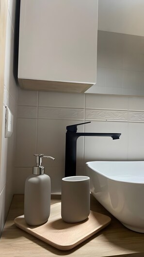 A bathroom with a white sink, a black faucet, and a wooden tray with two white containers. - Apartment 'Essential Suite Catania - Luxury' with Balcony, Wi-Fi and Air Conditioning (Catania)