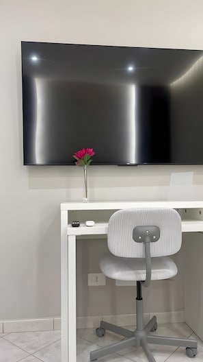 A modern office setup with a flat-screen TV mounted on the wall, a white desk, a striped office chair, and a vase with a single flower. - Apartment 'Essential Suite Catania - Luxury' with Balcony, Wi-Fi and Air Conditioning (Catania)
