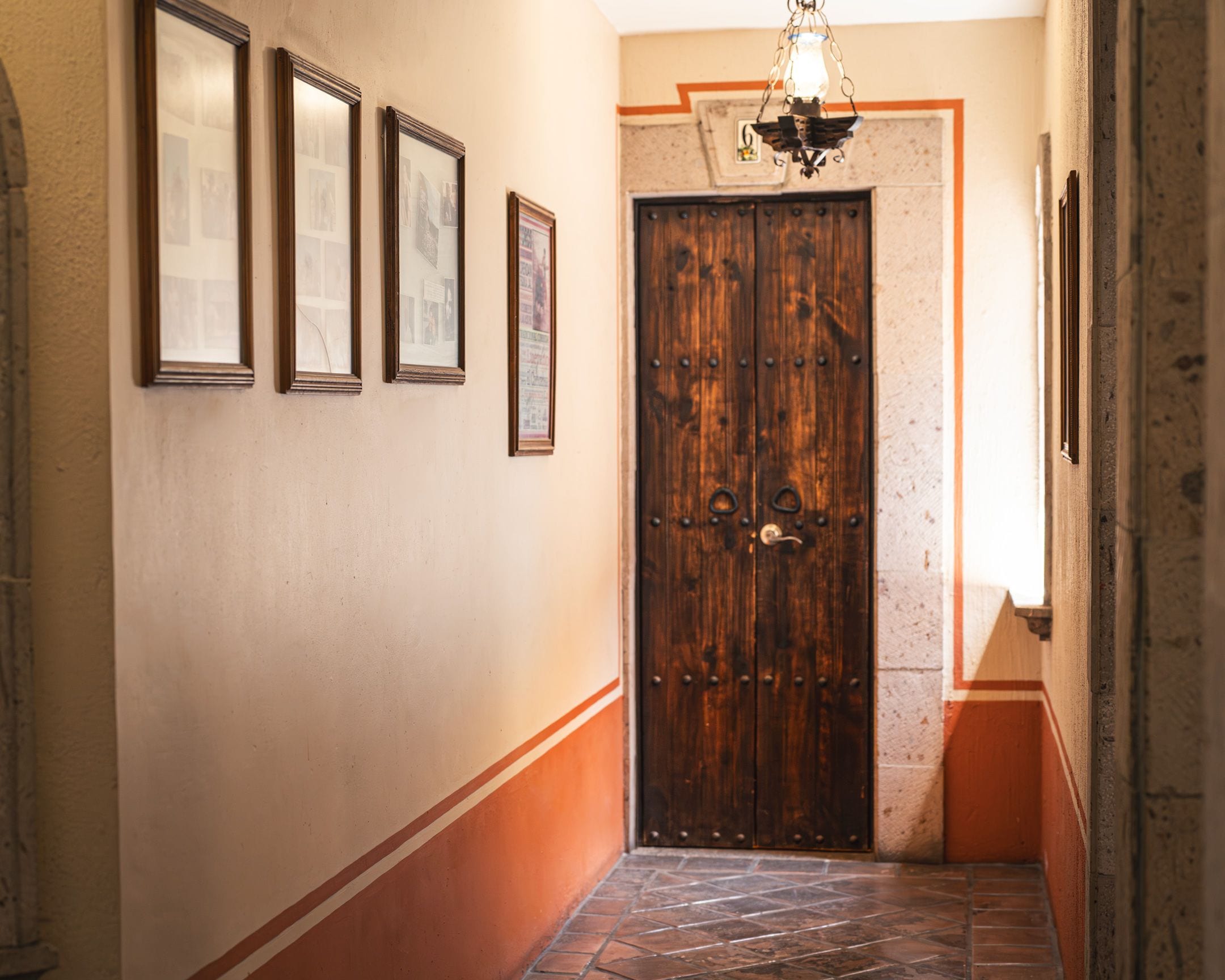 Un couloir avec une porte en bois, des tableaux encadrés accrochés au mur et un sol à motifs.