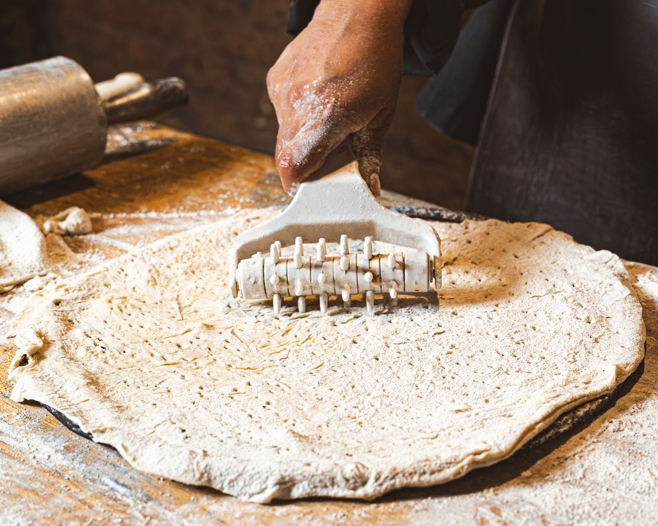 A hand using a pastry brush on a dough surface.