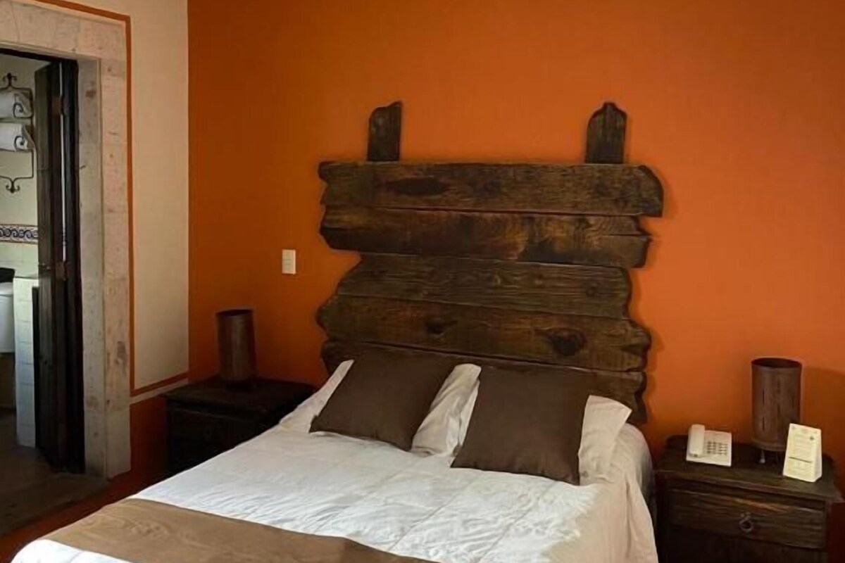 A bedroom with a wooden headboard, a bed with white bedding, a nightstand, and a bedside table with a lamp.