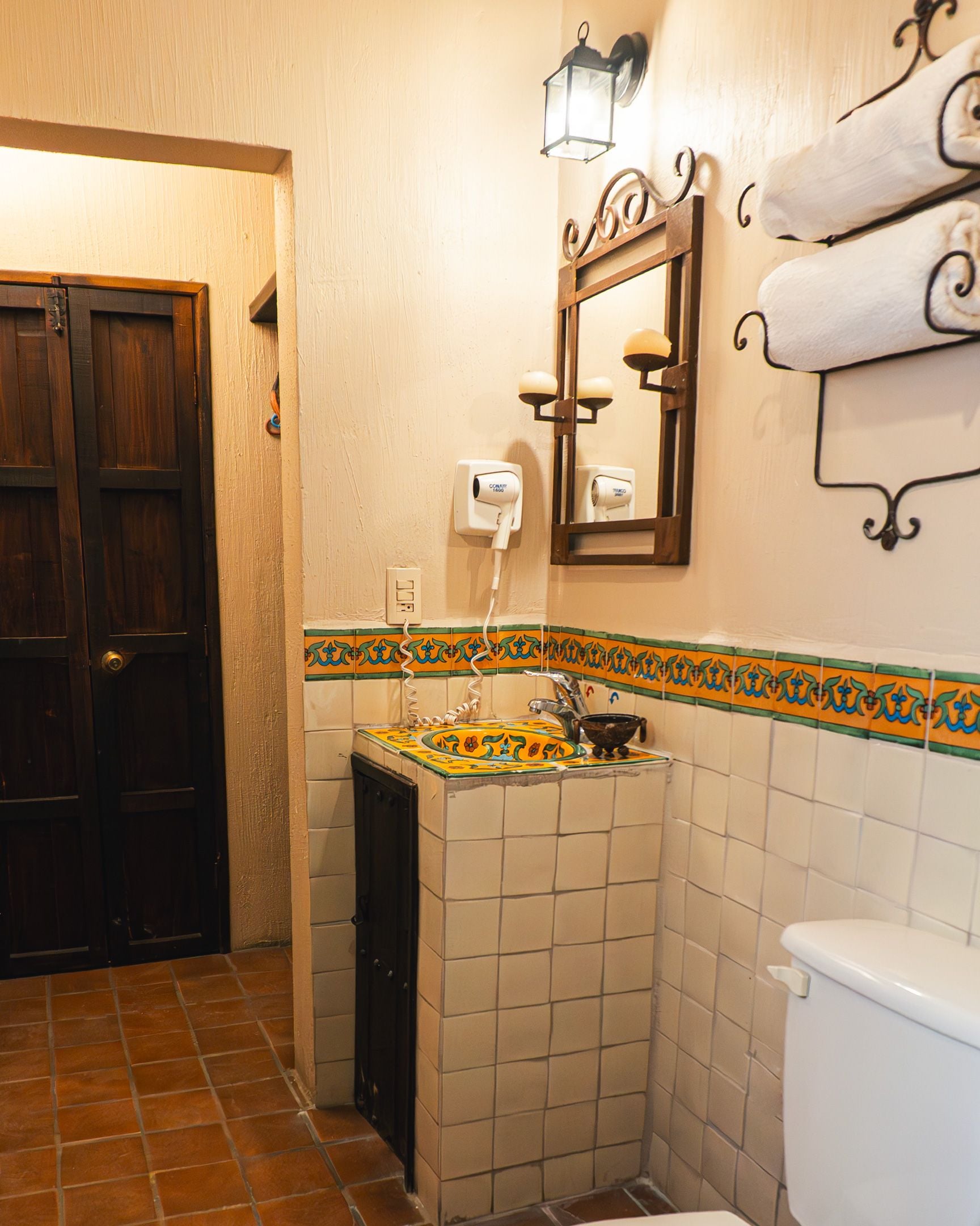 Une salle de bain avec un sol carrelé, un lavabo, des toilettes, un miroir et un porte-serviettes.