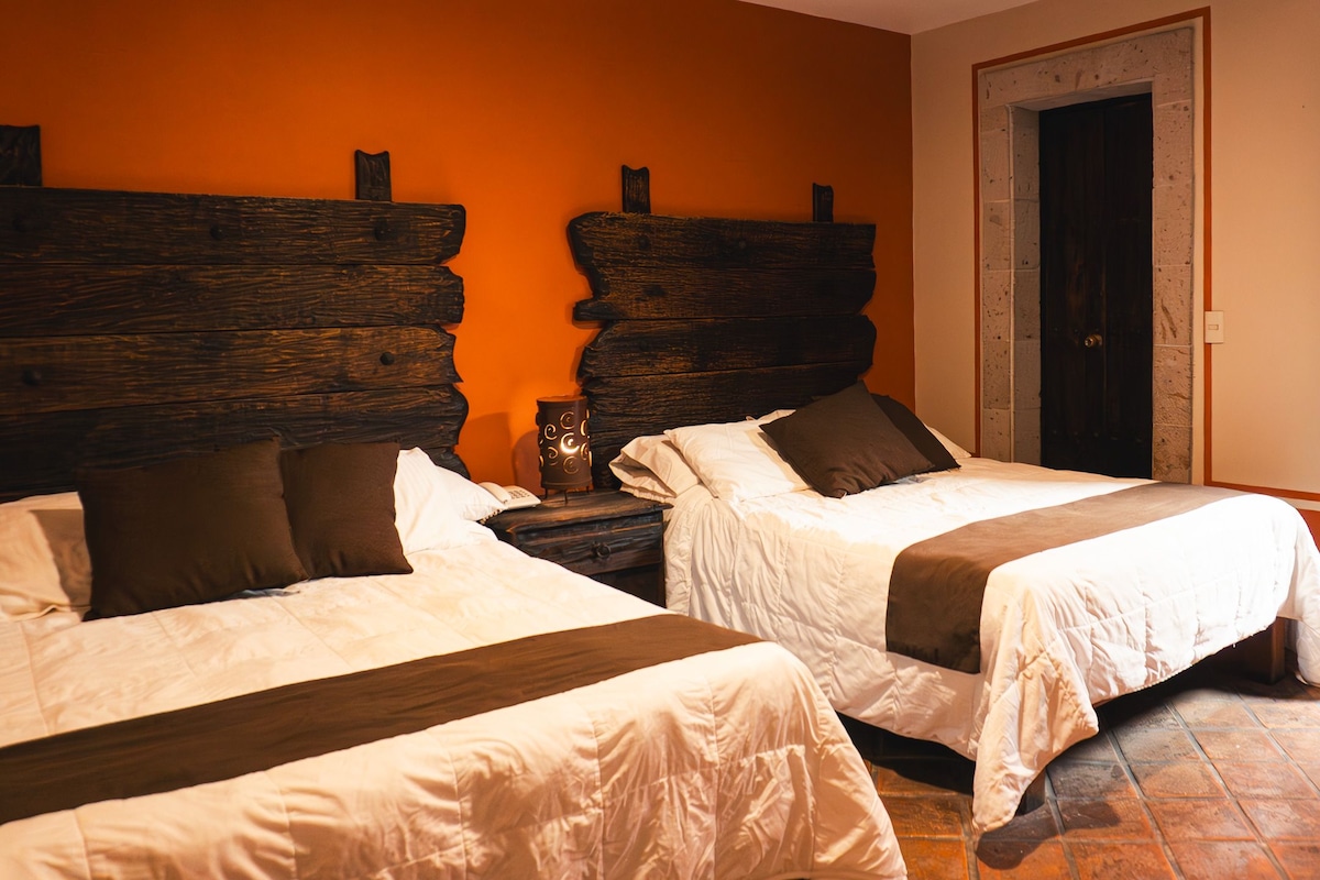 A hotel room with two beds, a wooden headboard, a nightstand, and a door.