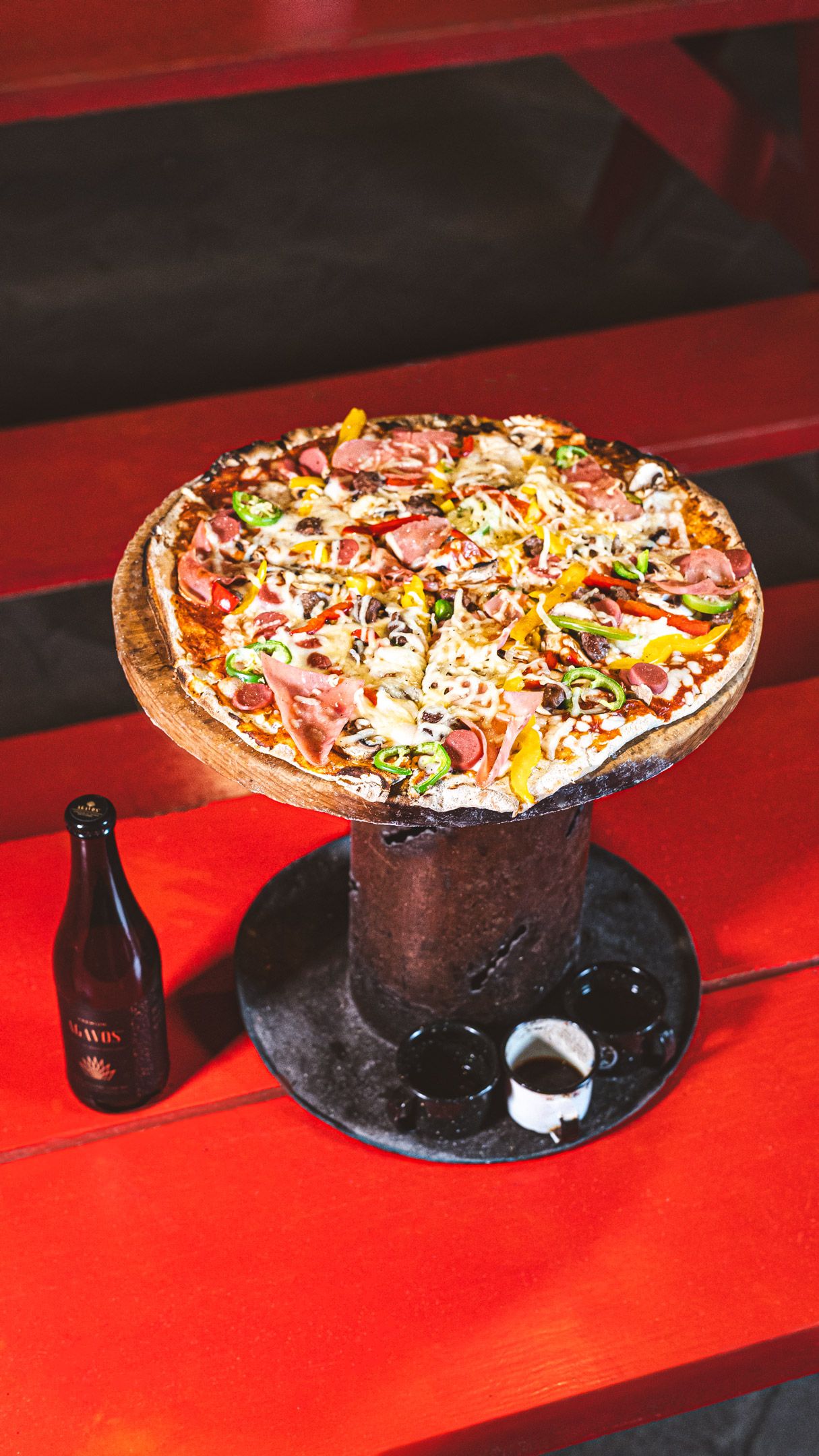 Una pizza sobre un soporte de madera con una botella al lado.