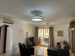 Un soggiorno con una TV a schermo piatto, due divani, una lampada da terra e una ventola a soffitto.