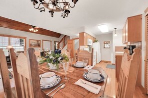 A dining area with a wooden table set for four, a chandelier, and a view of the kitchen. - Chill at Lakefront Lodge!  Clean, Serene, Comfort (Branson West)