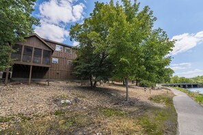 A rustic cabin with a balcony, surrounded by trees and a gravel path. - Chill at Lakefront Lodge!  Clean, Serene, Comfort (Branson West)
