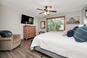 A bedroom with a bed, a dresser, a chair, a ceiling fan, a window, and a TV on the wall. - Chill at Lakefront Lodge!  Clean, Serene, Comfort (Branson West)