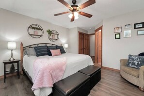 A bedroom with a bed, bedside tables, a bench, a ceiling fan, and a chair. - Chill at Lakefront Lodge!  Clean, Serene, Comfort (Branson West)
