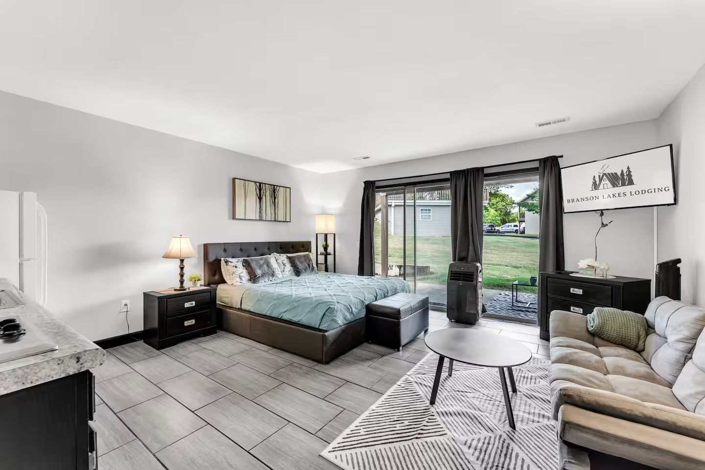 A modern bedroom with a bed, bedside tables, a nightstand, a sofa, a coffee table, and a view of the outdoors.
